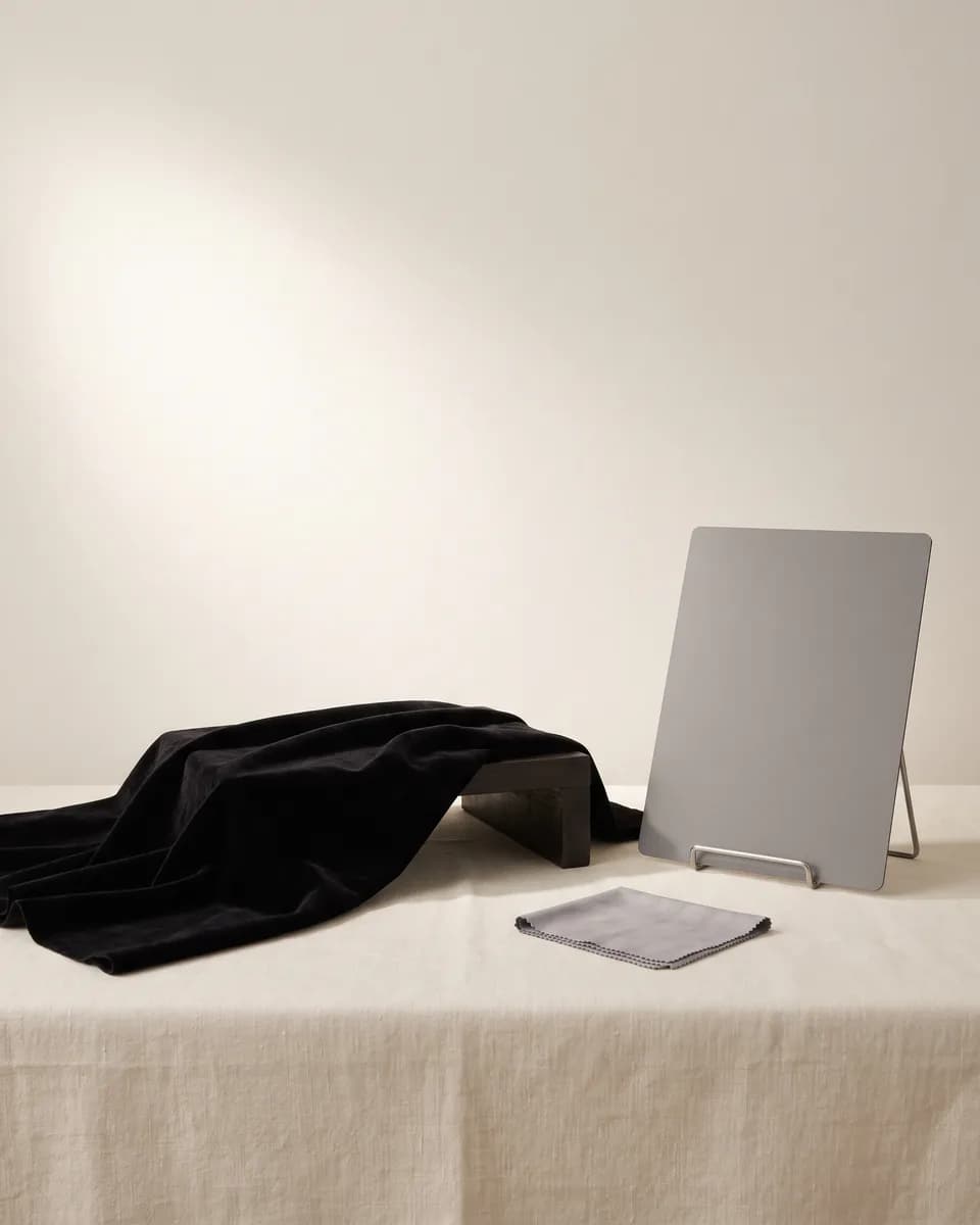 Black velvet draped over a small riser on a linen table, a grey card and a folded cloth beside it, under one soft light